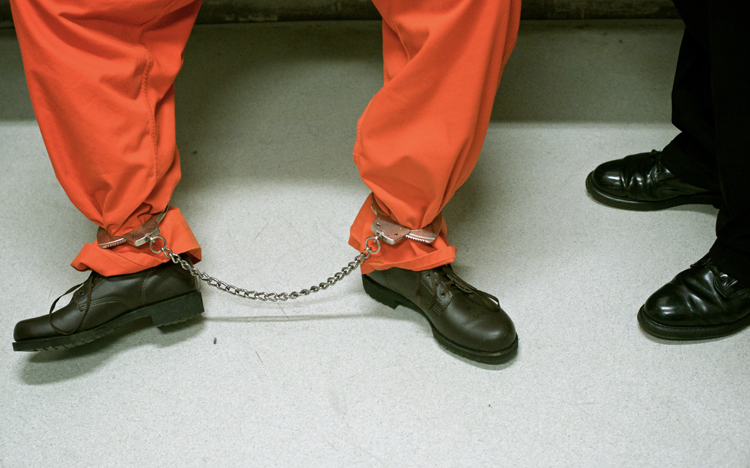 inmate in shackles waiting on a bench