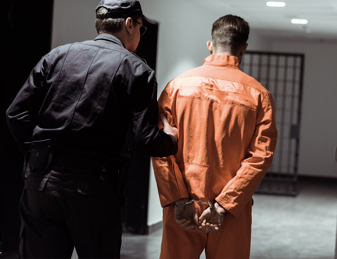 guard leading inmate in orange and handcuffs down a hall.